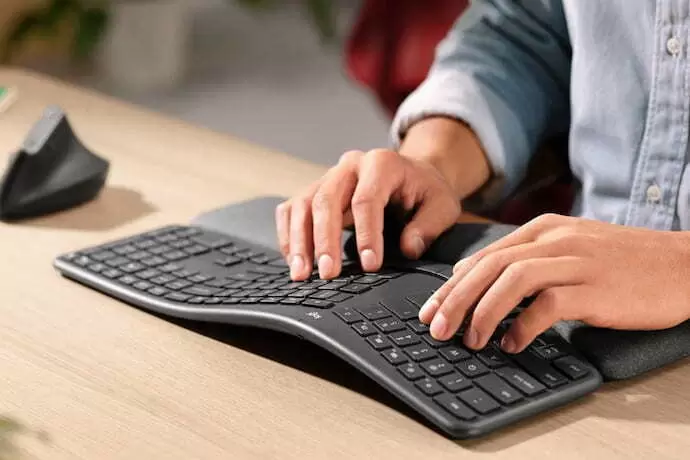 Pessoa mexendo em um teclado ergonomico grande com as duas mãos.