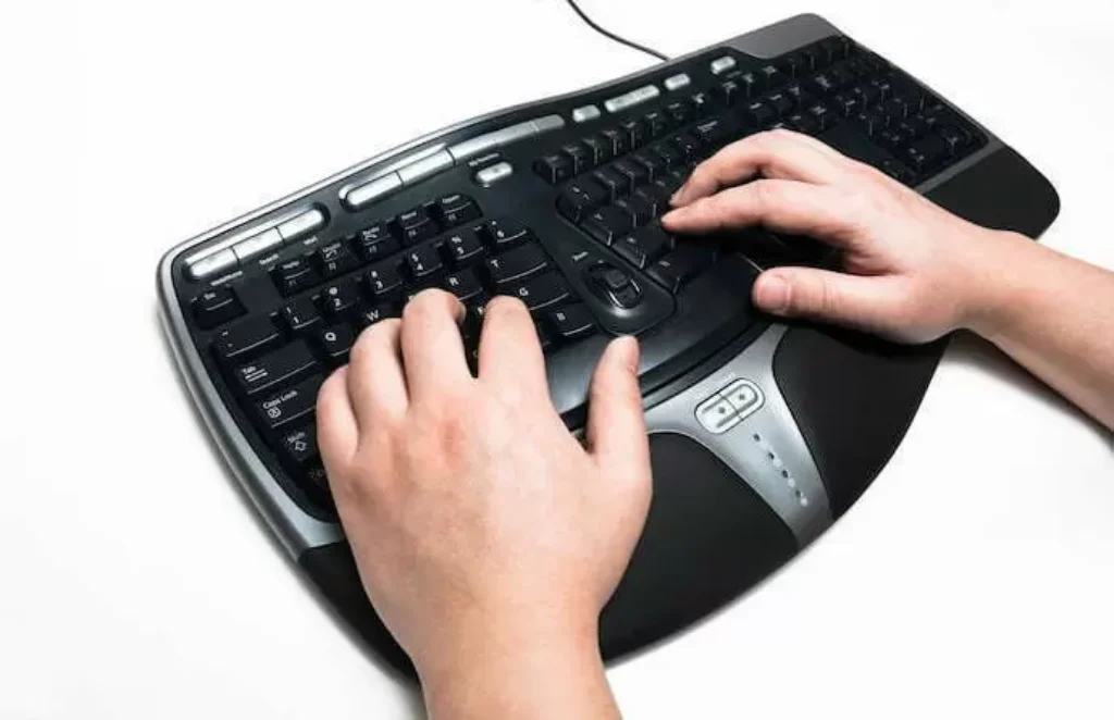 Uma pessoa mexendo em um teclado ergonômico com as cores preto e cinza. 