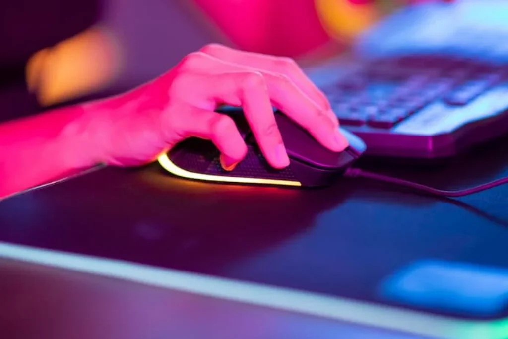 UMA PESSOA CLICANDO EM UM MOUSE GAMER PRÓXIMO DE UM TECLADO.