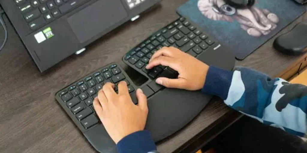 Pessoa escrevendo em um teclado ergonomico preto. 