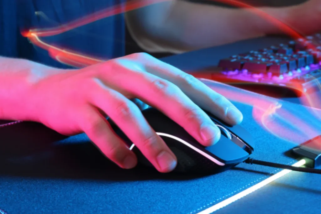 Uma pessoa clicando em um mouse gamer em cima de um mouse pad gamer.
