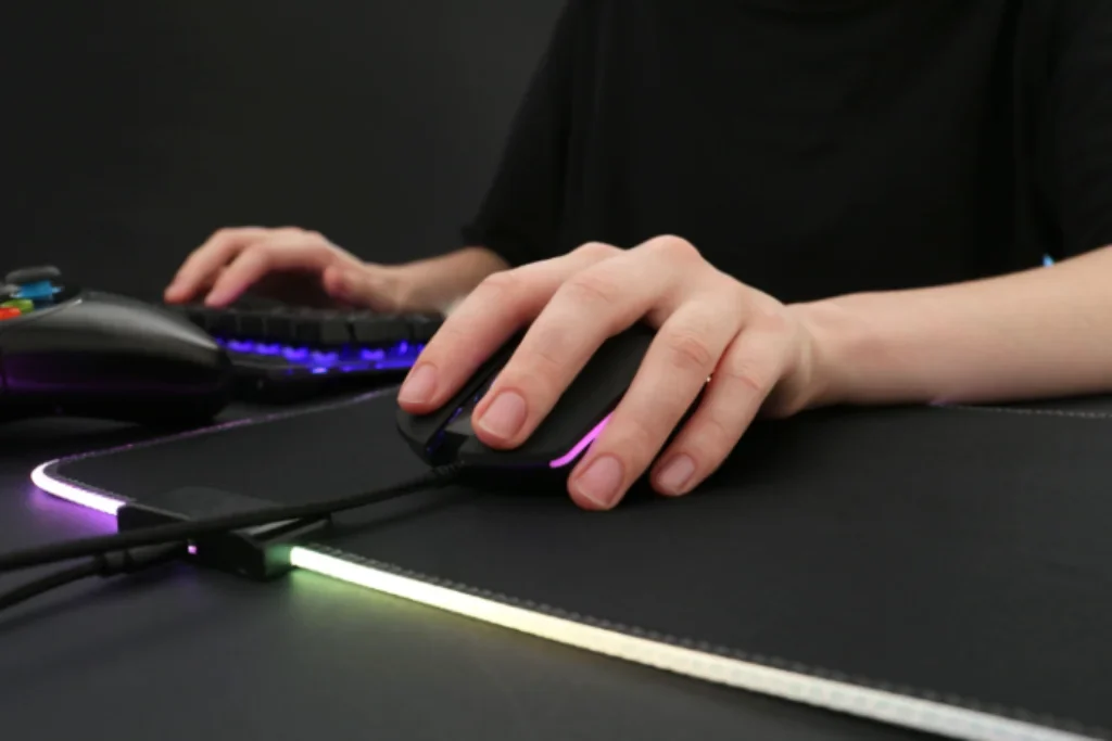 Uma pessoa jogando no PC com as mãos em um teclado e mouse gamer.