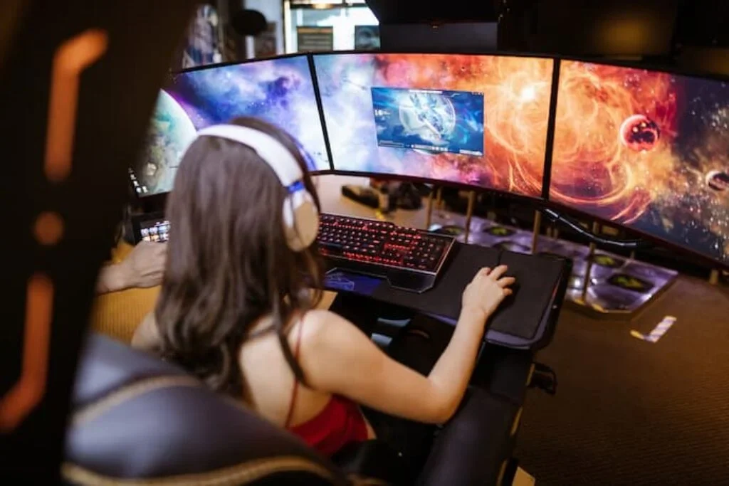 Uma menina jogando com três telas de computador.