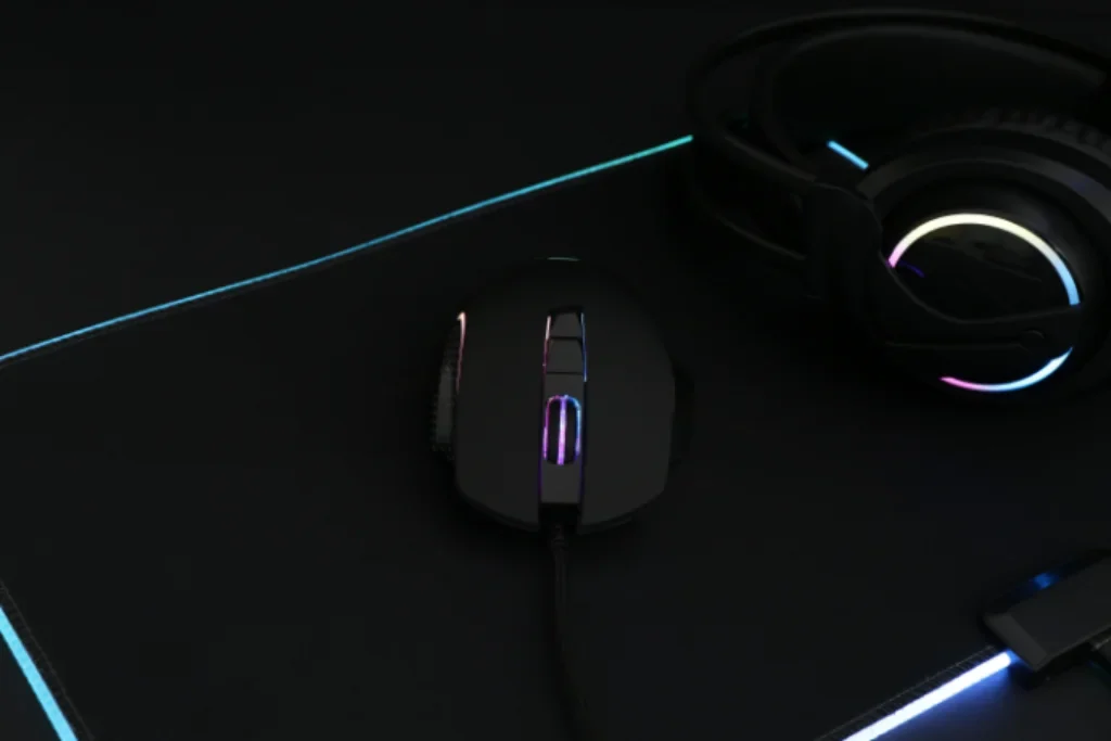 Um mouse gamer em cima de um mouse pad gamer com RGB e ao lado um fone gamer.
