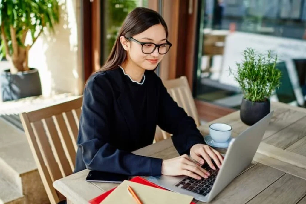 Uma pessoa jovem trabalhando em um notebook sentada em uma mesa.