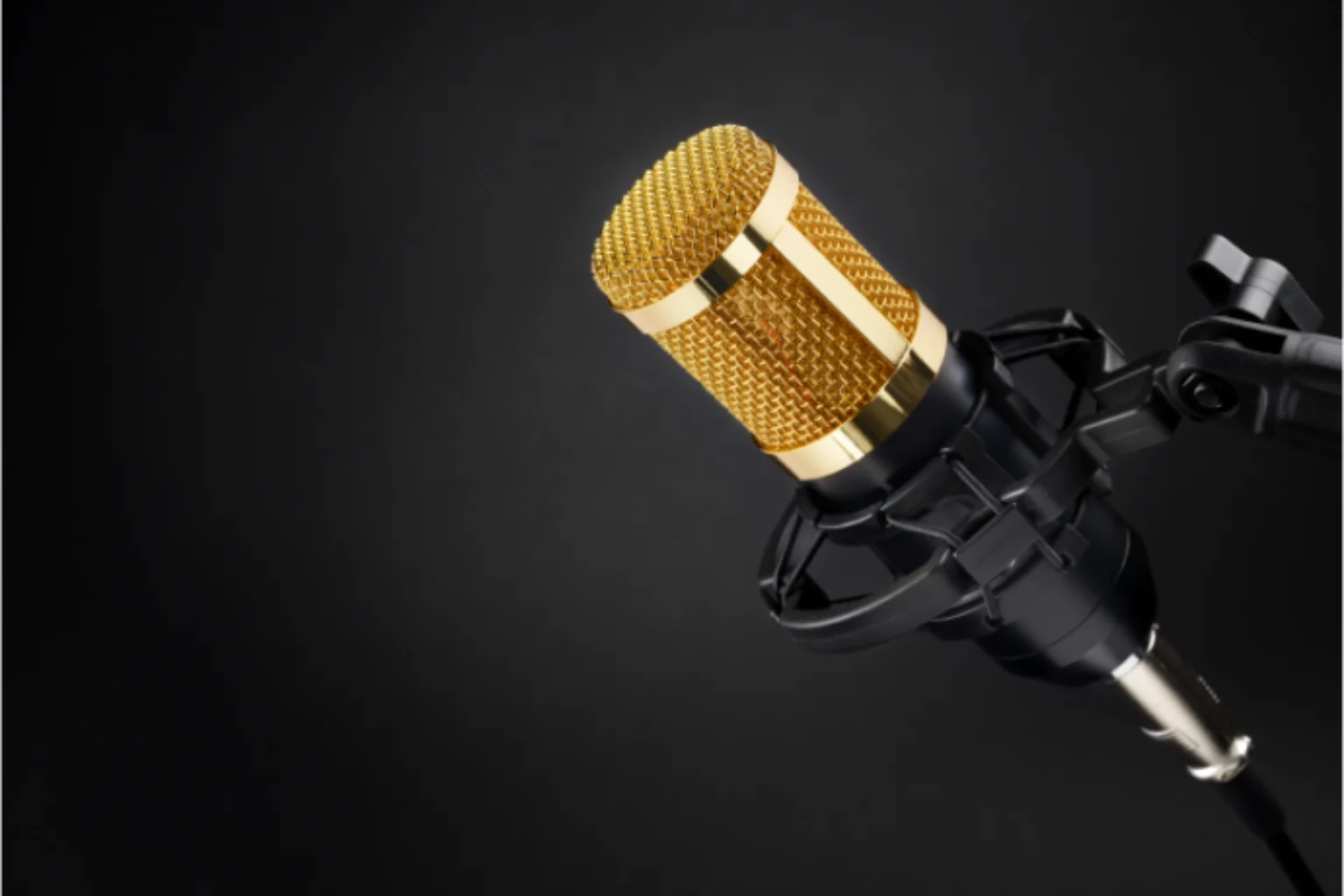 Microfone condensador dourado sobre um fundo cinza.